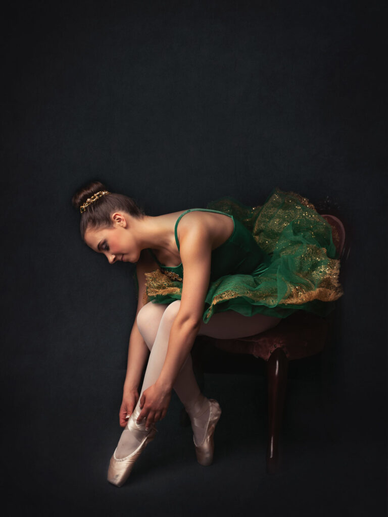 a ballerina in a green outfit tying her toe shoes
